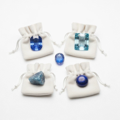 Various blue gemstones (sapphire, aquamarine, lapis lazuli) arranged in individual soft pouches on a white background
