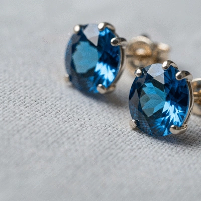 Close-up of a pair of sparkling blue gemstone earrings on a soft, light-colored cloth, with gentle light reflecting off the gems, no text, no words, no typography, clean image