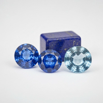 Assortment of polished blue gemstones, including sapphire, lapis lazuli, and aquamarine, arranged artfully on a light background
