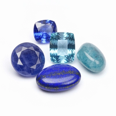Assortment of polished blue gemstones like sapphire, aquamarine, and lapis lazuli on a white background