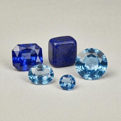Assortment of polished blue gemstones, including sapphire, lapis lazuli, and aquamarine, arranged on a soft, neutral-colored fabric