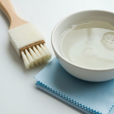 Close-up of cleaning tools for gemstones: a soft brush, a small bowl with warm soapy water, and a lint-free cloth on a bright, clean surface, no text, no words, no typography, no labels, clean image