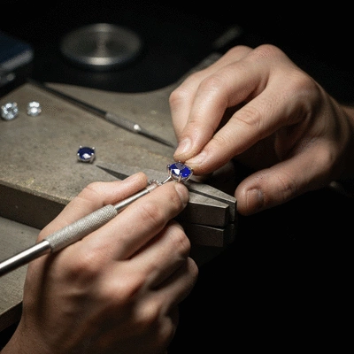 Jeweler's hands carefully placing a sapphire into a custom ring setting, with tools in the background