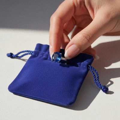 A hand gently placing a blue gemstone ring into a soft jewelry pouch, symbolizing careful storage.